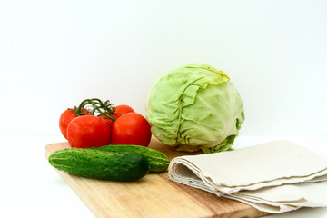 On a cutting board, tomatoes on a branch, cucumbers, a linen towel, cabbage, a head of red onions. Concept - vegetable diet, cooking soup.