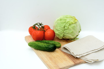 On a cutting board, tomatoes on a branch, cucumbers, a linen towel, cabbage. Concept - vegetable diet, cooking soup.