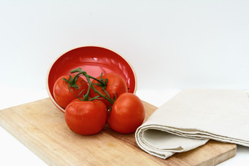 Tomatoes are lying on a cutting board on a green branch against a red ceramic cover and a linen towel. Isolated objects. Concept - vegetable diet