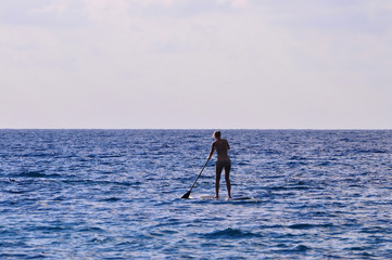 Silhouette unidentified girl stand up paddle boarding at the beach - Image holiday/vacation concept