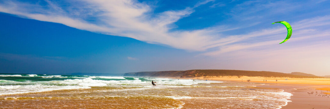 Surfers in Praia da Bordeira beach near Carrapateira, Portugal. Kiteboarder kitesurfer athlete performing kitesurfing kiteboarding tricks. Praia da Bordeira is popular location for surfing. Portugal