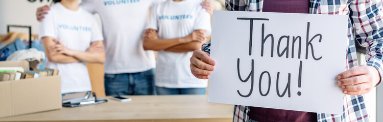 panoramic shot of man holding card with thank you inscription while standing near volunteers