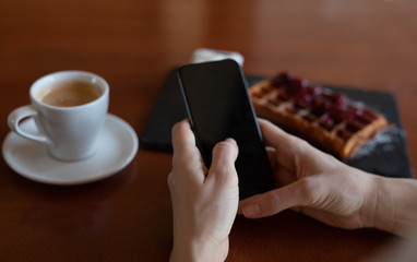 Woman typing on her phone while sitting in the cafe (close up of the hands and the phone)
