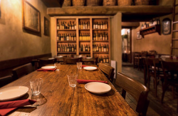 Focus on plates and water glass inside retro restaurant with wooden vintage furniture, plates, wine bottles. Sets of empty stylish cafe, bar or trattoria