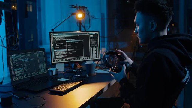 cybercrime, hacking and technology concept - asian male hacker in headphones with coding on laptop computer screen wiretapping or making cyber attack and drinking coffee in dark room at night
