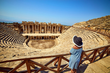 Back view of woman traveler in hat looking at amazing Amphitheater ruins in ancient Hierapolis,...