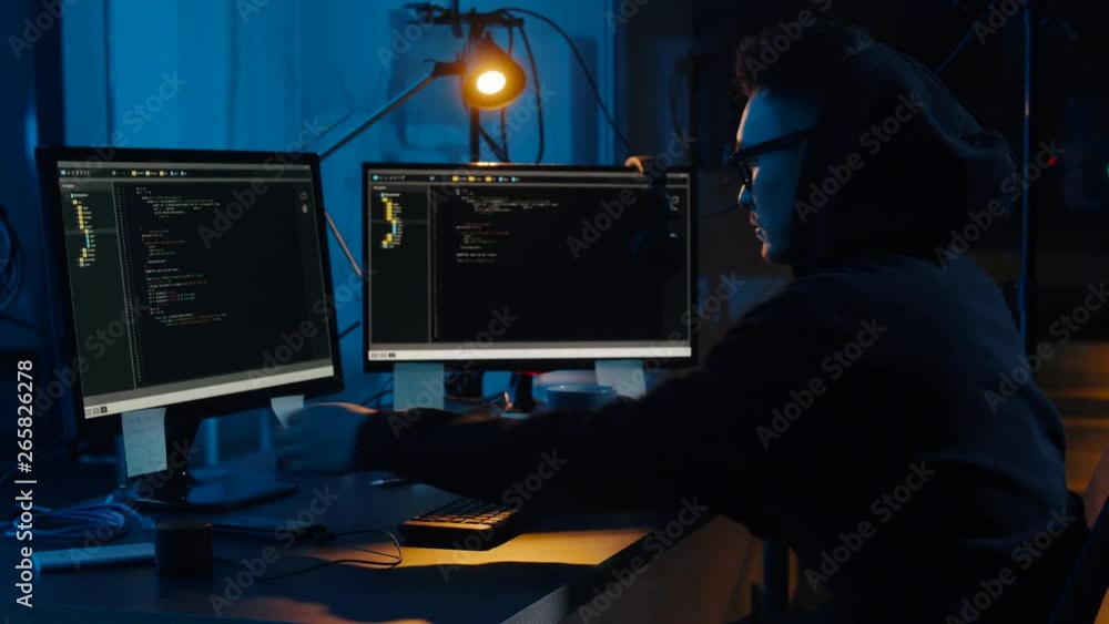 Poster cybercrime, hacking and technology concept - asian male hacker in glasses and hoodie using computer 