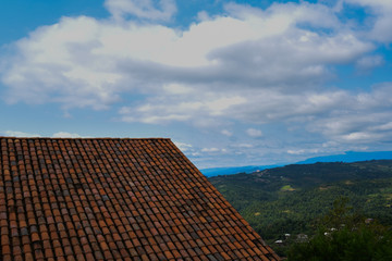 View of mountain scenery in medieval Motsameta monastery complex near Kutaisi, Georgia. The roof is covered with ancient red tiles on the background of the mountains. Old roof in front of blue sky.