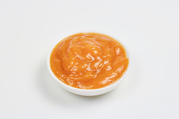 Orange sauce in white plate on white background.