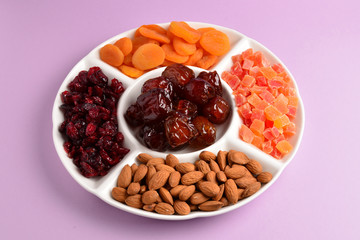 Mix of dried fruits and nuts on a white plate. Apricot, almond, raisin, dates fruit. On a lilac background. Space for text or design.