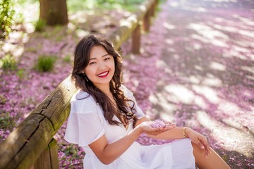 A young beautiful Asian woman in a white dress walks in a flowered park. Sakura. Blooming trees.