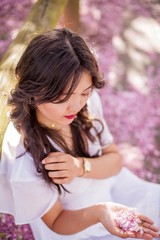 A young beautiful Asian woman in a white dress walks in a flowered park. Sakura. Blooming trees.