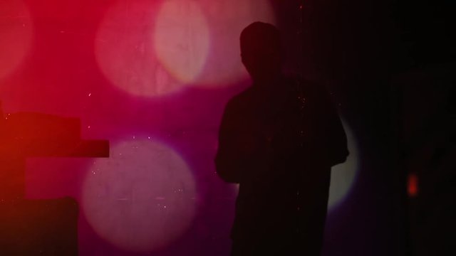 Silhouette of young stylish man rapper drinking beer dancing hip hop on stage. Man&rsquo;s shadow on the screen.