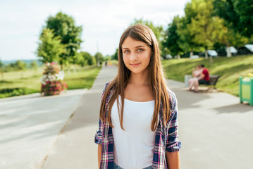 Girl schoolboy in a shirt, in the summer in city stands on the road. Happy smiling, resting after school. Long hair white t-shirt. Free space for text.