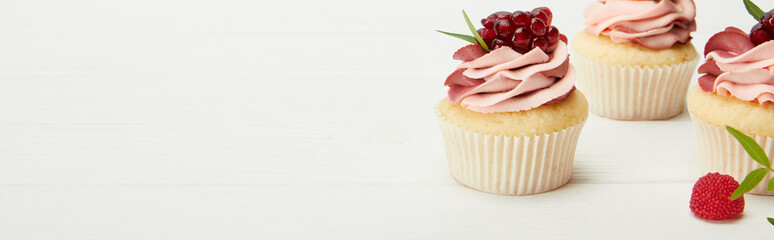 panoramic shot of sweet cupcakes with garnet on white surface