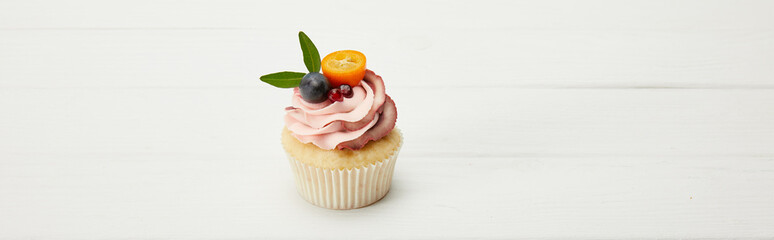panoramic shot of cupcake with kumquat, garnet and grape on white surface