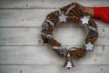 Christmas holiday background. Celebration theme. Celebration concept, free space for text. Female hand with christmas wreath with silver christmas decor and ivy on white rustic background. Toned image