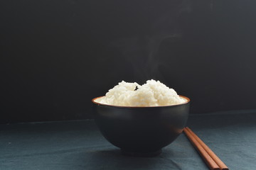 bowl of steamed white rice with chopstick and black background
