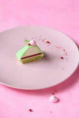 Pyramid - Contemporary Green Tea Matcha Mini Mousse Cake with strawberry jelly, covered with green velvet spray and decorated with pink meringue cookie, on light pink background.