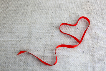Red heart ribbon isolated on brown cloth background.