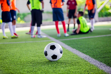 soccer ball on green artificial turf with blurry soccer players standing