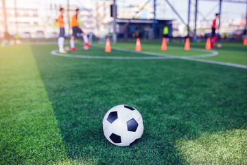 football on green artificial turf with blurry soccer team training, blurry kid soccer player jogging between marker cones