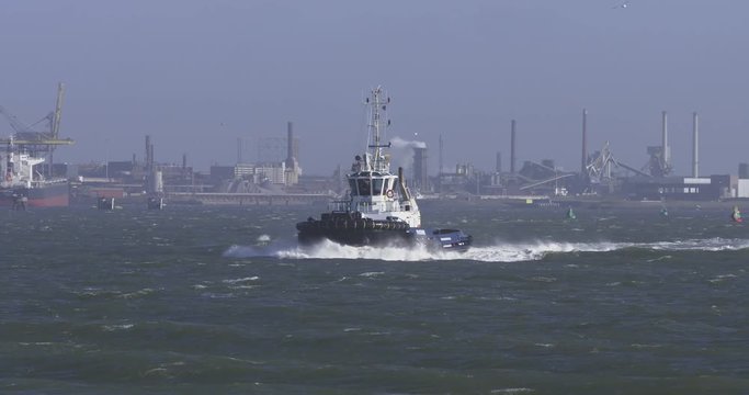 tugboat in rough sea ploughing through the hig waves. Huge bowwave. Industrial environment