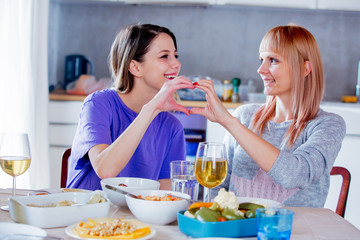 Two women drinking wine in glass at home.