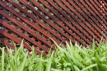 Rustic wooden latticework in the shape of a corridor on a stone floor and green grass.