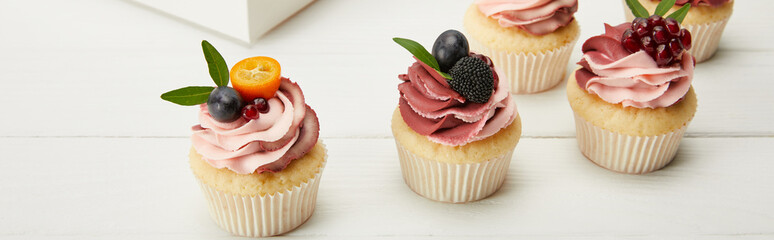 panoramic shot of cupcakes with fruits and berries on white surface