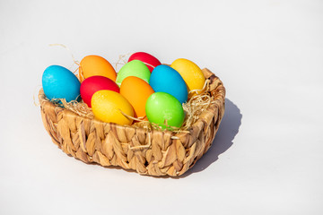 Gefärbte Ostereier im Korb im Sonnenlicht vor weißem Hintergrund