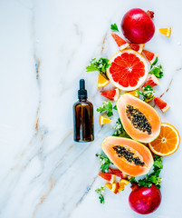 Fresh cut papaya with ceeds, garnets, oranges near black bottle on marble surface. Above view