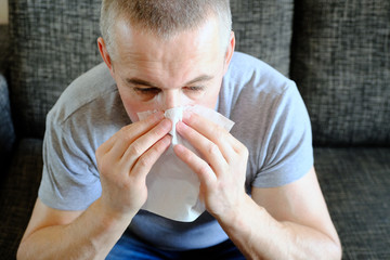 A man with a paper handkerchief near his nose. Allergies, spring blooms. Reaction to pollen, allergic syndrome.