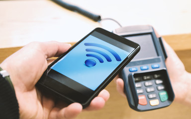 Pay by smartphone through the terminal. Man with smartphone mobile payment in store.
