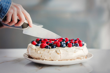 female hands of the pastry chef cut cream pie with blueberries and raspberries on a table