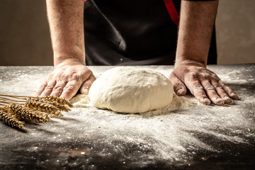 Beautiful and strong men's hands knead the dough from which they will then make bread, pasta or pizza. A cloud of flour flies around like dust. Food concept