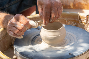 Potter cuts the edges of pottery with thread on spinning wheel. Outdoor workplace