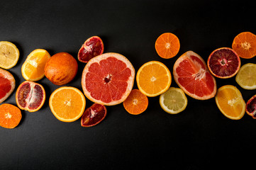 Top view, flat lay. Many slices colorful citrus on a black background. Fruits lined up in the...