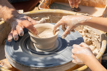 A man with a child molds a vase on a potter's wheel. Outdoor potter lessons