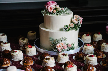 White wedding cake with pink flowers and greens on a festive table with French pastry. close up of cake. Sweet table.