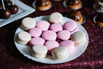 Obraz na płótnie Canvas Delicious sweet pink, purple, pastel, beige macaroons in a plate on a violet background. Festive sweet table with baking.