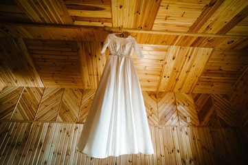 Fashionable beautiful classic lace silk wedding dress hanging on hanger in hotel wooden room. morning preparation wedding concept. vintage wedding gown.