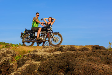 Obraz premium Young couple on a motorcycle on on rocky ground. Happy guy and girl travelling on a motorbike.