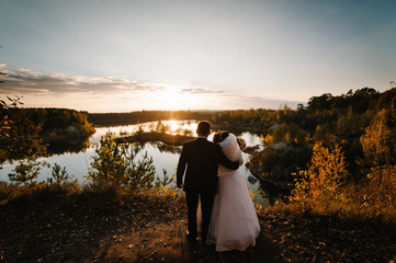 The wedding couple is standing back by the lake and looking at the landscape. Autumn nature and...