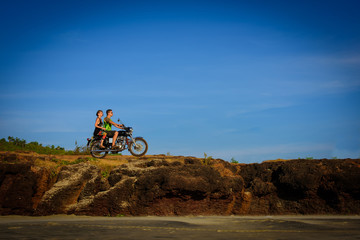 Naklejka premium Young couple on a motorcycle on on rocky ground. Happy guy and girl travelling on a motorbike.