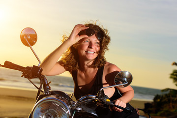 Fototapeta na wymiar Portrait of a beautiful woman sitting on motorcycle, smiling and holding sunglasses on the forehead.