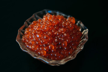 Red caviar in glassware on a black background close up. Gourmet food.