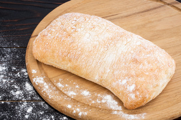 Loaf of ciabatta bread on a cutting board on the dark wooden table