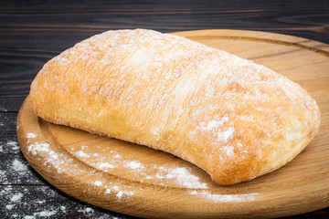Loaf of ciabatta bread on a cutting board on the dark wooden table