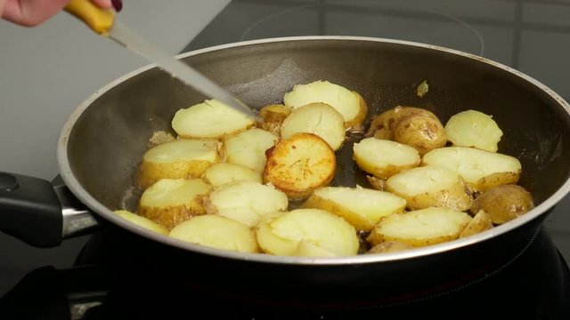 Close up. Potatoes in a frying pan fried in butter. A woman's hand turns the pieces over with a knife. Food concept